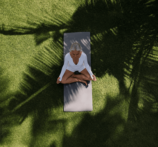 Woman meditating outdoors under palm tree shadows