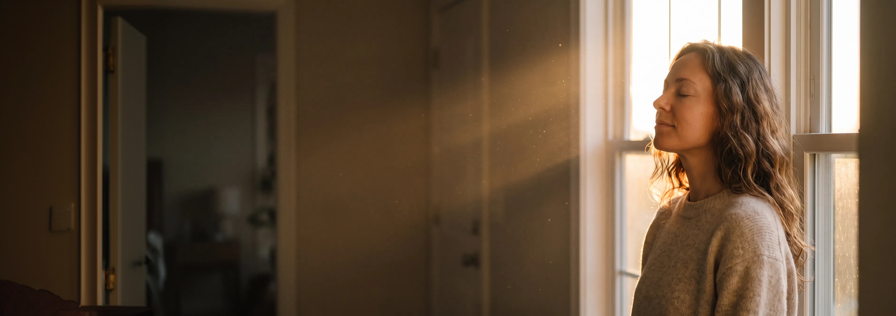 Woman enjoying warm morning sunlight by a window